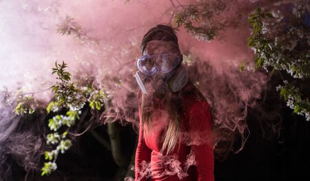Young beautiful girl portrait in a mask with degree of protection posing in twilight of spring garden.の写真素材