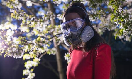 Young beautiful girl portrait in a mask with degree of protection posing in twilight of spring garden.の写真素材