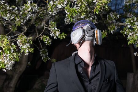 Young man portrait in mask with degree of protection posing in twilight of spring garden.の写真素材