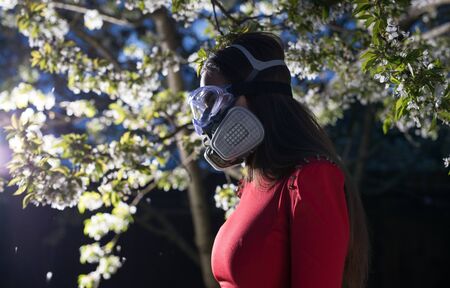 Young beautiful girl portrait in a mask with degree of protection posing in twilight of spring garden.の写真素材