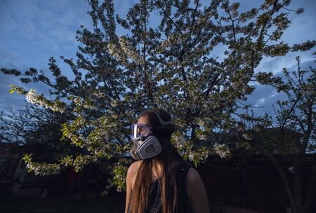 Young beautiful girl portrait in a mask with degree of protection posing in twilight of spring garden.の写真素材