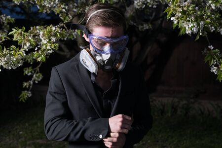 Young man portrait in mask with degree of protection posing in twilight of spring garden.の写真素材