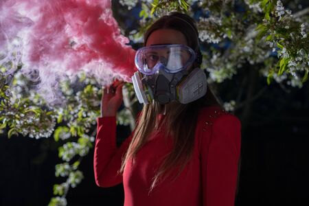 Young beautiful girl portrait in a mask with degree of protection posing in twilight of spring garden.の写真素材