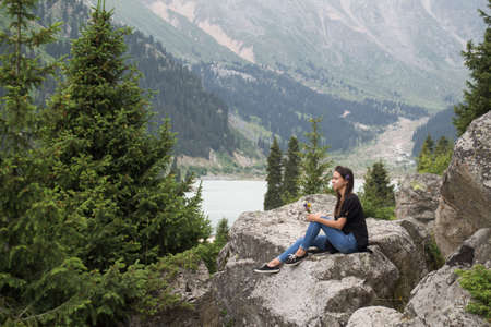cute girl sitting on a rock holding flowers on a background of mountainsの写真素材