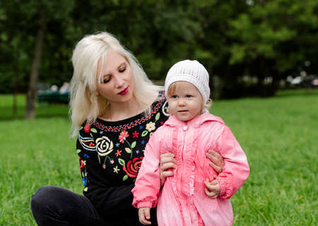 Young mother is holding a little girl for a walk in the parkの写真素材