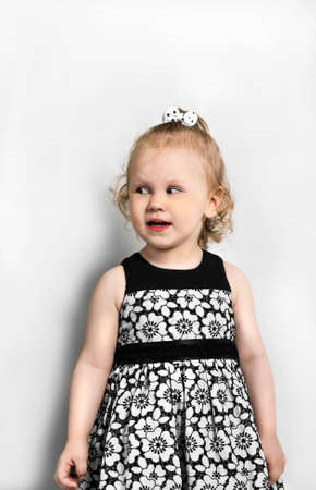 Little girl in a black and white dress stands looks aside, is interested in somethingの写真素材