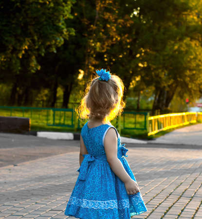 Little girl in beautiful blue dress looking at the sunsetの写真素材