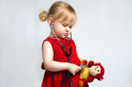 Little girl in a doctor costume with stethoscope in hand, play monkeyの写真素材