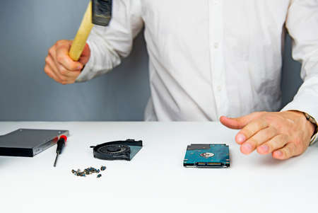 The man with the hammer swings on the hard drive to the laptop to break it on the table to disassemble the laptopの写真素材