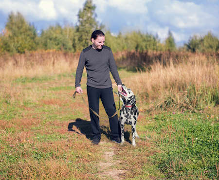 young man walking a dog Dalmatian outdoors in the park greenの写真素材