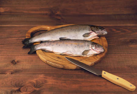 Fresh raw fish trout is two pieces on the board for cutting food on a wooden table in rustic style near the knifeの写真素材