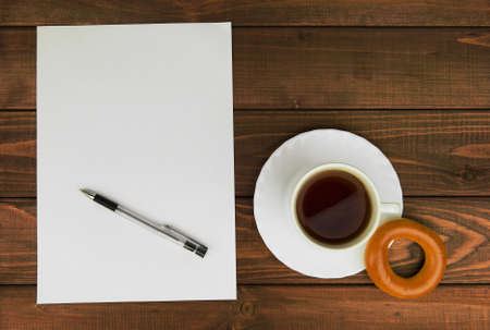 White paper on a wooden table next to a cup of tea, bagels and ballpoint pen - concept with space...