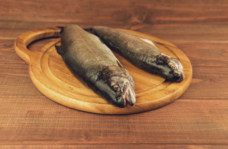 Fresh raw fish trout is two pieces on the board for cutting food on a wooden table in rustic style near the knifeの写真素材