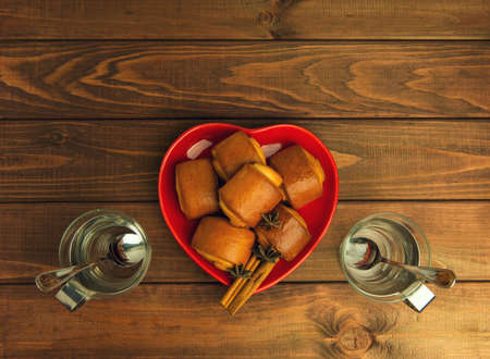 Empty cup of glass with a metal handle and cinnamon rolls on a plate standing on a wooden tableの写真素材