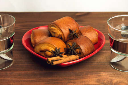 Empty cup of glass with a metal handle and cinnamon rolls on a plate standing on a wooden tableの写真素材