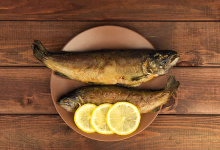 On the wooden table is a plate with two baked fish trout with lemonの写真素材