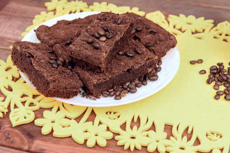 On a wooden table on yellow  plate of chocolate truffle cake, a lot of coffee beans