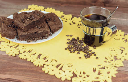On a wooden table on yellow napkin glass cup of coffee with a spoon and a plate of chocolate truffle cake, a lot of coffee beansの写真素材