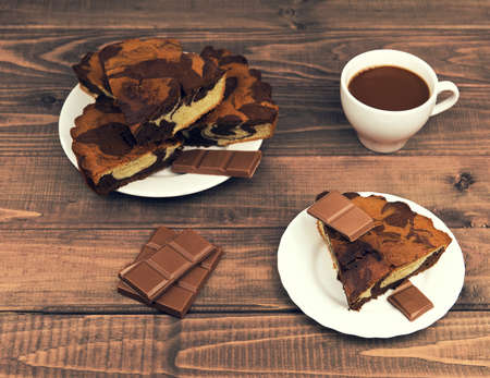 Marble cake in white plate cut into pieces a la carte, standing next to a cup of hot chocolate and milk chocolate tile pieces on a wooden table in the rural-rustic styleの写真素材