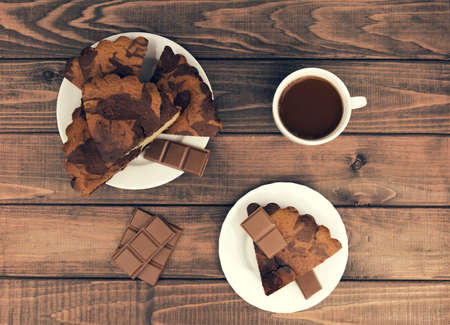 Marble cake in white plate cut into pieces a la carte, standing next to a cup of hot chocolate and milk chocolate tile pieces on a wooden table in the rural-rustic styleの写真素材