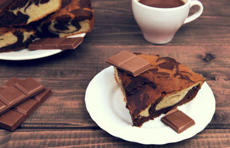 Marble cake in white plate cut into pieces a la carte, standing next to a cup of hot chocolate and milk chocolate tile pieces on a wooden table in the rural-rustic styleの写真素材