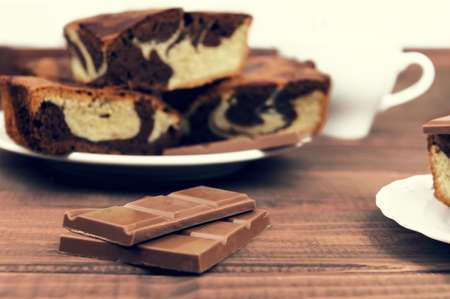 Marble cake in white plate cut into pieces a la carte, standing next to a cup of hot chocolate and milk chocolate tile pieces on a wooden table in the rural-rustic styleの写真素材