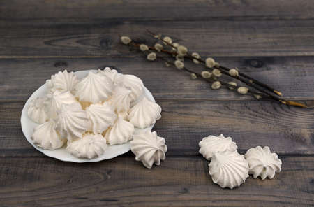 On the wooden table is a white porcelain plate with cakes and meringues bouquet of flowers willowの写真素材