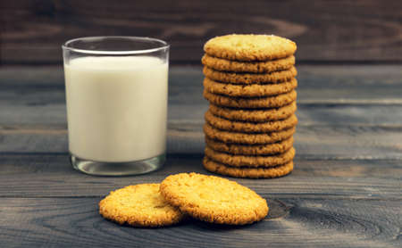 On the rustic wooden table is breakfast - a red glass plate with homemade oat biscuits and a glass of milkの写真素材