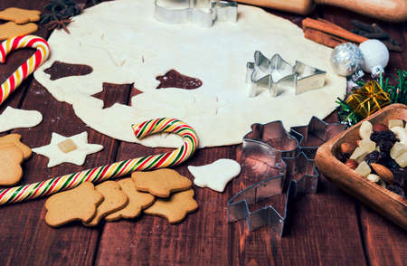 On a wooden desk background Christmas composition - candy cane, dough figurines, Christmas-tree branch Christmas balls, raisins, nuts, cinnamon sticks, cookies, star anise, mandarins bump roll out the dough layer plungerの写真素材