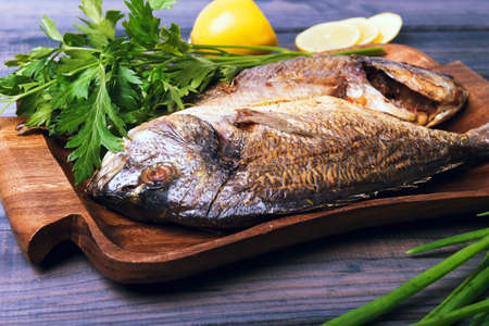 On a wooden table plate with two roasted carp fish dorado with parsley, chives and lemon.の写真素材