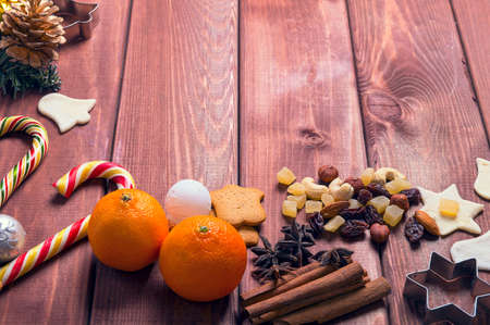 On a wooden desk background Christmas composition - candy cane, dough figurines, Christmas-tree branch Christmas balls, raisins, nuts, cinnamon sticks, cookies, star anise, mandarins bumpの写真素材