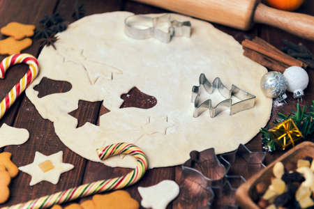 On a wooden desk background Christmas composition - candy cane, dough figurines, Christmas-tree branch Christmas balls, raisins, nuts, cinnamon sticks, cookies, star anise, mandarins bump roll out the dough layer plungerの写真素材
