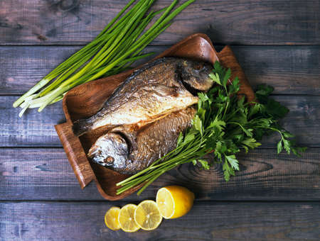 On a wooden table plate with two roasted carp fish dorado with parsley, chives and lemon.