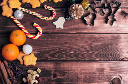 On a wooden desk background Christmas composition - candy cane, dough figurines, Christmas-tree branch Christmas balls, raisins, nuts, cinnamon sticks, cookies, star anise, mandarins bumpの写真素材