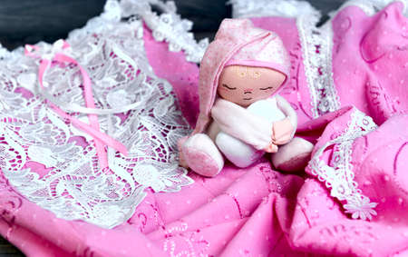 On a wooden table delicate pink nightgown with lace and soft toy doll man sleep in a pink cap with a pillow in his handsの写真素材