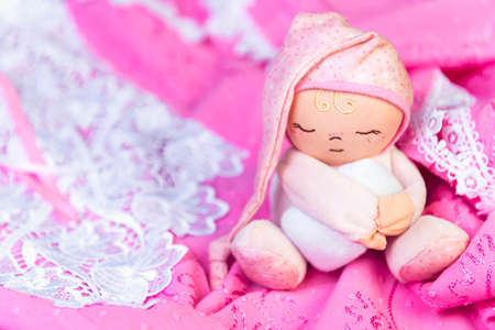 On a wooden table delicate pink nightgown with lace and soft toy man sleep in a pink cap with a pillow in his handsの写真素材