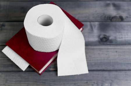 On a gray wooden background hardcover red cover to read and white embossed roll of toilet paper for use in the toiletの写真素材