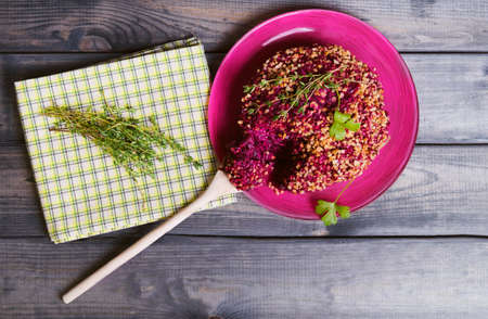 On a wooden table glass dish with beetroot salad, napkin, towel with herbs thyme, celery, wooden spoon and ground nutsの写真素材