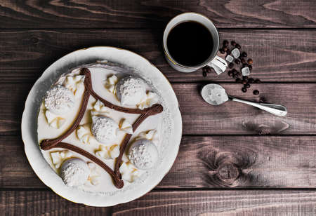 On a wooden table delicacy - a saucer with a piece of cake and a cup of meringue with coffee beans...