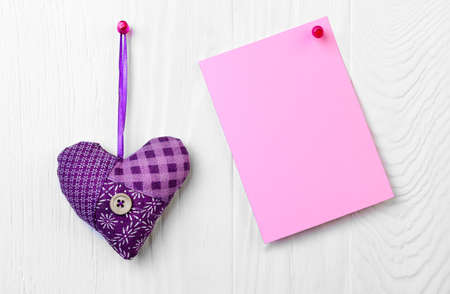 On a white background wooden wall pinned buttons sewn fabric heart and an empty letter Valentine's...