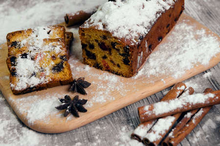 On a wooden desk background Christmas stollen Stollen, powdered sugar like snow, cinnamon sticks, star aniseの写真素材