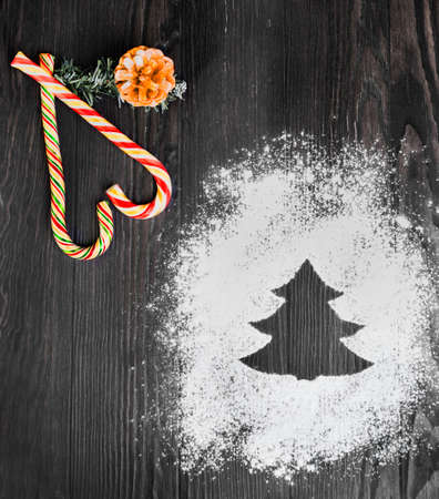 On a brown wooden desk background scattering of flour and powdered sugar in the form of Christmas...
