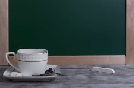 On a wooden table in vintage style square white porcelain cup and saucer set with coffee, coffee beans, spoon, chalk drawing boardの写真素材