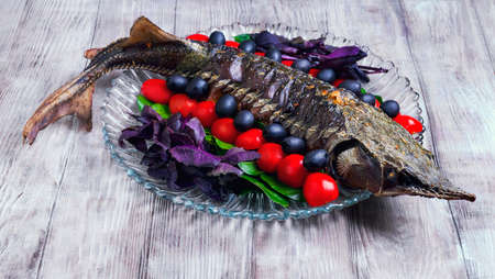On a light wooden background vintage style with a celebratory dinner baked fish sturgeon on a large...