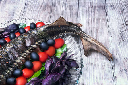 On a light wooden background vintage style with a celebratory dinner baked fish sturgeon on a large...