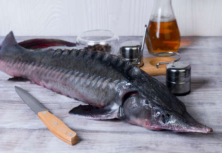 On the wooden background large clear glass dish with a large of whole raw fish sturgeon