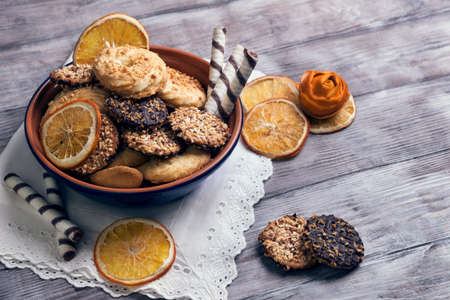 On a light wooden background blue ceramic bowl with cookies, decorated with a dried orange slices, rose from the orange peel, chocolate rolls, white napkin with laceの写真素材
