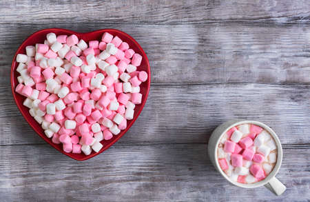 On a black wooden table in rustic style red heart-shaped plate with marshmallows, there is an empty space for your text, congratulations on Valentine's Dayの写真素材