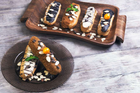 On a light wooden table tray and glass dish with cakes eclairs, mint, berries Physalis, almonds,...