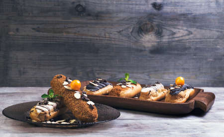 On a light wooden table tray and glass dish with cakes eclairs, mint, berries Physalis, almonds, chocolateの写真素材